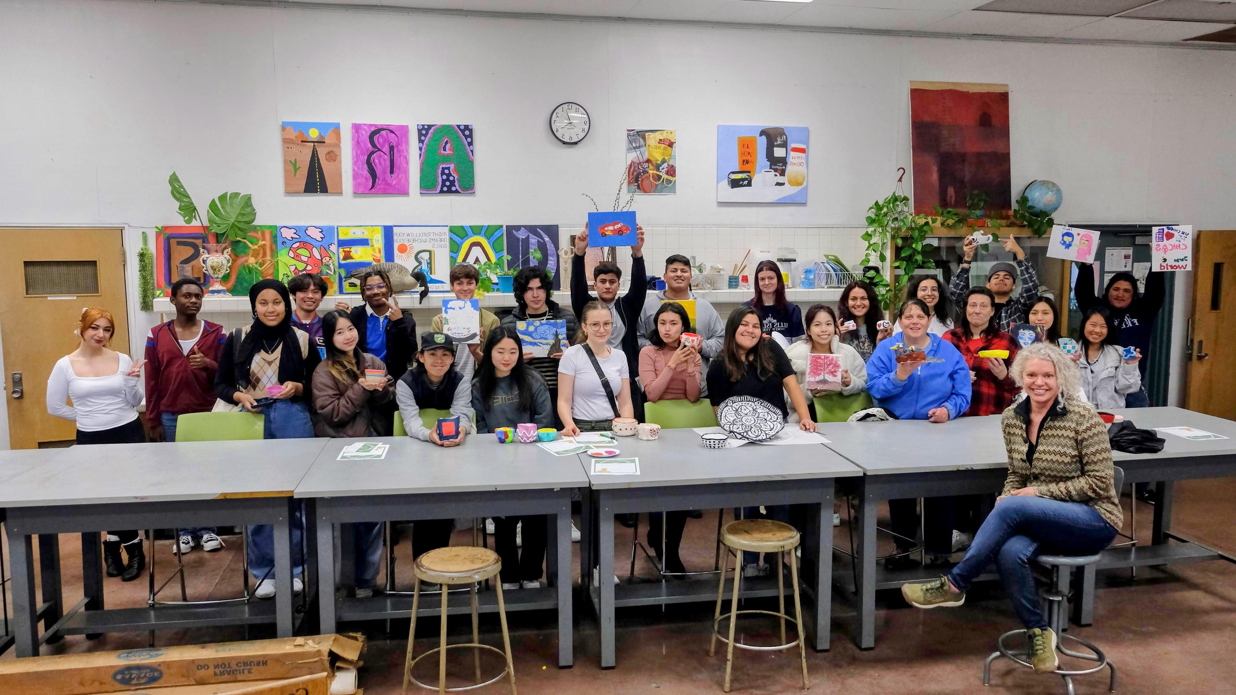 group of students in an art studio showing their art pieces